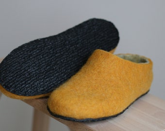 May include: A pair of yellow wool slippers with black rubber soles. The slippers are on a wooden surface.