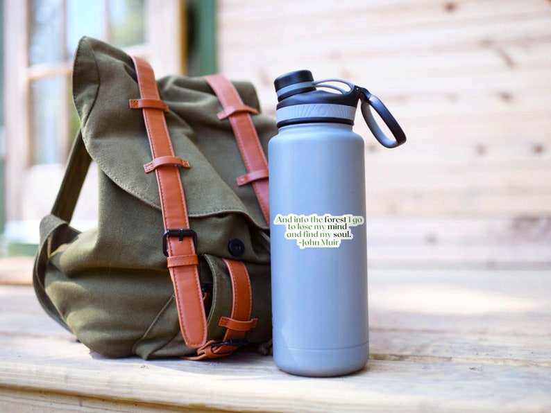 May include: A gray stainless steel water bottle with a black lid and handle. A sticker with the quote "And into the forest I go to lose my mind and find my soul. -John Muir" is on the bottle.