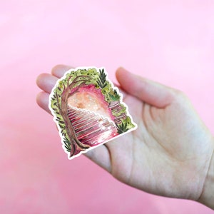 May include: A whimsical sticker featuring a watercolor illustration of a staircase leading into a glowing portal framed by a tree and foliage. The sticker has a white border and is held in a hand against a pink background.