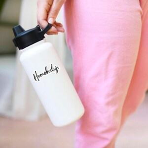 Pu&ograve; includere: Bottiglia d'acqua bianca con tappo nero e scritta nera "Homebody."
