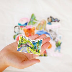 May include: A watercolor sticker featuring a scenic view of a road winding through a forest with a tunnel in the distance. The sticker has the text "Blue Ridge Parkway" printed on it.