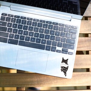 以下が含まれることがあります： キーボードの右上の角に黒と白のフクロウのステッカーが貼られた銀色のラップトップコンピューターです。