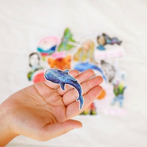 Op de afbeelding: Een blauwe walvis sticker met een sterrenpatroon. De sticker wordt in een hand gehouden.