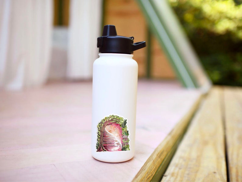 May include: A white insulated water bottle with a black cap and a whimsical sticker. The sticker features a watercolor illustration of a doorway framed by a tree with a staircase leading into a pinkish light.