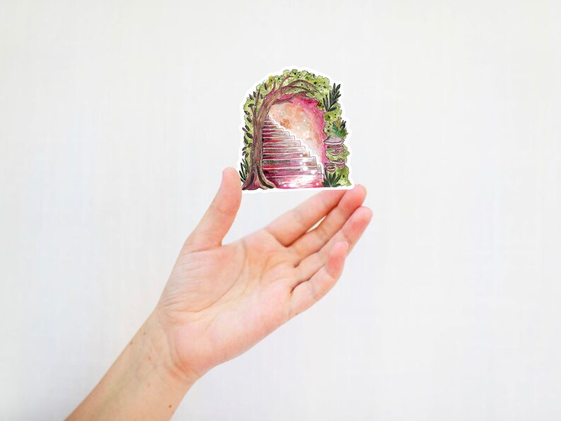 May include: A sticker featuring a watercolor illustration of a stone staircase leading into a glowing archway, framed by a tree and foliage. The sticker is held in a hand against a white background. The artwork has a fantasy theme.