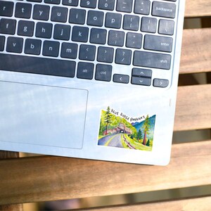 May include: A silver laptop computer with a sticker of a watercolor painting of a road through a tunnel with the text "BLUE RIDGE PARKWAY" on it.
