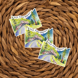 May include: Three watercolor stickers featuring a scenic view of the Blue Ridge Parkway. Each sticker features a winding road leading to a tunnel with lush green trees and a blue sky in the background. The text "Blue Ridge Parkway" is written in black cursive on each sticker.