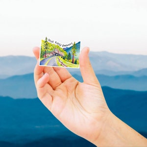 May include: A watercolor illustration of a scenic road with a tunnel, surrounded by trees and mountains. The text "Blue Ridge Parkway" is written in black at the top of the image.