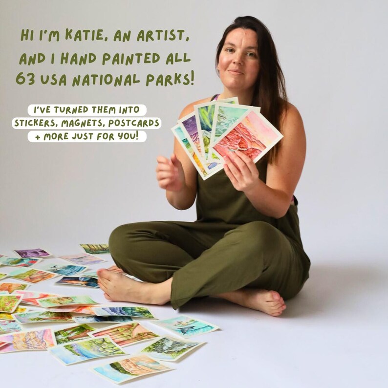 May include: A woman holding up watercolor paintings of national parks. The text reads "Hi I'm Katie, an artist, and I hand painted all 63 USA National Parks! I've turned them into stickers, magnets, postcards + more just for you!"