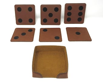 May include: Six brown leather dice coasters with black dots, and a brown leather tray with a tan felt lining.