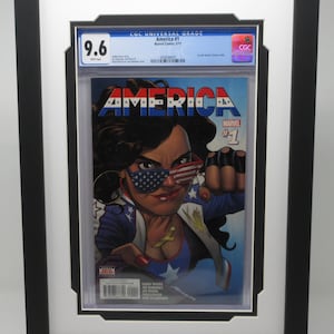 May include: A graded comic book in a black frame with a white mat. The comic book cover features a woman with black hair wearing a red, white, and blue costume and sunglasses. The comic book is titled "America #1" and is graded 9.6 by CGC.