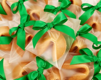 Puede incluir: Un grupo de galletas de la fortuna envueltas en bolsas de celofán transparentes atadas con lazos de cinta de satén verde.
