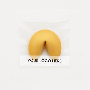 May include: A golden-brown fortune cookie in a clear plastic wrapper. The cookie has a curved shape, and the wrapper has a white label with the text "YOUR LOGO HERE" in black.