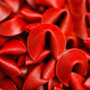 Peut inclure: Gros plan sur une pile de biscuits chinois rouges vifs. Les biscuits sont à différents stades d'ouverture, leurs formes incurvées et leurs surfaces texturées étant clairement visibles. L'image est bien éclairée, soulignant la couleur vibrante et les détails des biscuits.