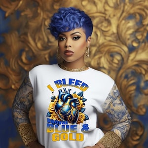 以下が含まれることがあります： ロイヤルブルーとゴールドのハートのグラフィックと「I Bleed Royal Blue & Gold」というテキストが書かれた白いTシャツです。