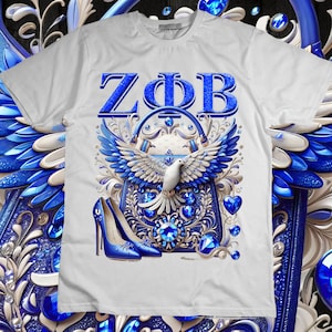 May include: White t-shirt with a blue and gold design featuring the letters "ZOB" and a dove with outstretched wings. The design also includes a purse with jewels and a blue high-heeled shoe.