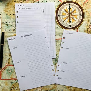 Op de afbeelding: Drie witte pagina's met gestreept papier en gaten aan de linkerkant. De pagina's zijn gelabeld met "Maand van", "Week van" en "Prioriteiten van deze week". De pagina's liggen op een bruine en gele kaart.
