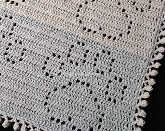 May include: A two-toned crochet blanket featuring a geometric pattern in beige and light gray. The textile displays a repeating openwork design with a decorative scalloped edge made of small loops. The text "Wicklow Designs" is visible in white.