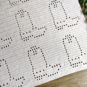 May include: White crochet baby blanket with a repeating pattern of small squares and circles. The blanket is made with a soft, lightweight yarn and is perfect for cuddling.