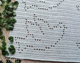 May include: A light blue crochet blanket featuring a repeating heart pattern created with openwork stitches. The textile has a consistent horizontal row structure with a visible grid-like design forming the heart shapes throughout the fabric.