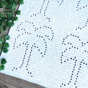 May include: White crochet blanket with a geometric pattern of black circles. The blanket has a fringe border.