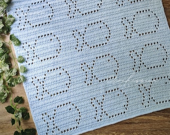May include: A light blue crochet blanket featuring a repeating pattern of the letters X and O created with openwork stitches. The textile has a consistent grid-like arrangement of these characters across the entire surface of the square fabric.