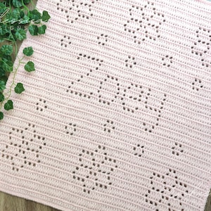 Puede incluir: Una manta de bebé de ganchillo rosa con un patrón repetitivo de pequeños círculos. La manta está hecha con un hilo suave y tiene un aspecto delicado y de encaje.