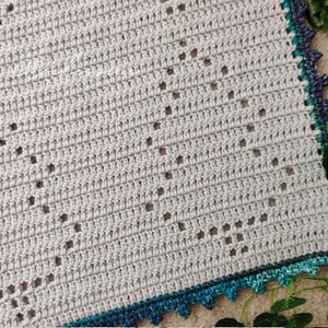 May include: A crocheted blanket with a gray center and a teal and blue border. The blanket has a diamond pattern with holes in the center.