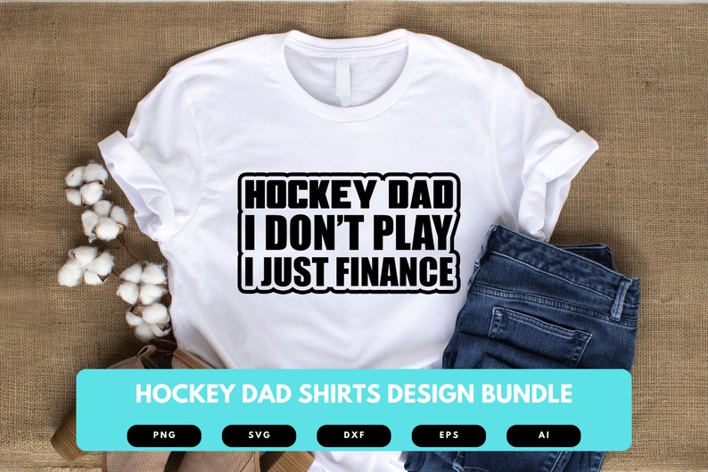 May include: White t-shirt with black text that reads "Hockey Dad I Don't Play I Just Finance". The shirt is on a brown burlap background with a pair of jeans and cotton balls.