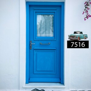 May include: A blue door with a window and a white door frame. A vintage blue pickup truck with a black license plate that reads "7516" is on the white wall next to the door.