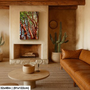 May include: A 32x48 inch (81x122cm) canvas print of a vibrant forest scene. The artwork features red-orange tree trunks with green foliage, displayed above a fireplace in a cozy living room setting. The room includes a brown leather sofa and a round wooden coffee table.