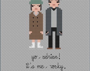 May include: Cross-stitch art featuring pixelated figures of a man and woman, with the text "yo, adrian! it's me, rocky." The woman wears a green hat and brown coat. The man wears a black hat and gray coat. A red heart is at the bottom.