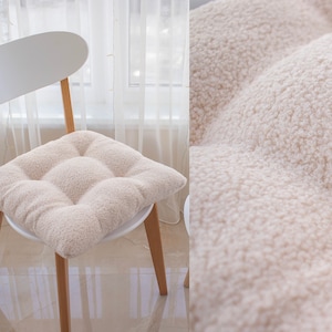 Könnte beinhalten: Ein weißer Stuhl mit einem hellbraunen, flauschigen Kissen. Das Kissen hat ein gestepptes Design mit vier Quadraten.