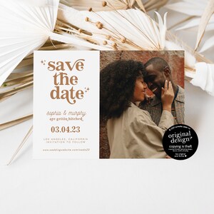 May include: A wedding announcement card with the text "save the date" in brown, along with the names "Sophia & Murphy" and the date "03.04.23". The card also features a photo of a couple. Dried plants are in the background.