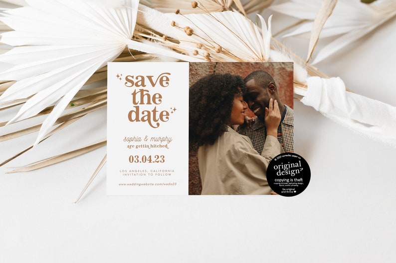 May include: A wedding announcement card with the text "save the date" in brown, along with the names "Sophia & Murphy" and the date "03.04.23". The card also features a photo of a couple. Dried plants are in the background.