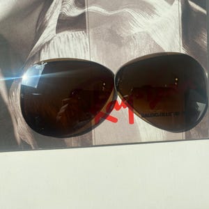 K&ouml;nnte beinhalten: Eine braun get&ouml;nte Fliegerbrille mit dem Ray-Ban-Logo auf dem oberen linken Glas und dem Schriftzug Bausch & Lomb auf dem unteren rechten Glas. Die tropfenf&ouml;rmigen Gl&auml;ser haben eine dunkle Verlaufsoptik und eine reflektierende Oberfl&auml;che.
