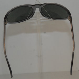 Pode incluir: Um par de &oacute;culos de sol cinzentos com lentes escuras. Os &oacute;culos est&atilde;o em um expositor.