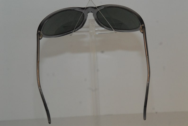 Pode incluir: Um par de &oacute;culos de sol cinzentos com lentes escuras. Os &oacute;culos est&atilde;o em um expositor.