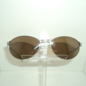 Puede incluir: Gafas de sol aviador plateadas con lentes marrones. Las gafas est&aacute;n en un expositor transparente.