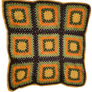 May include: A handmade crochet blanket featuring a patchwork design. The blanket is composed of nine square blocks in shades of brown, green, orange, and yellow. The border is a solid mustard yellow. The blanket is a cozy home decor item.
