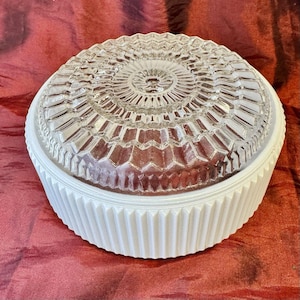 May include: A vintage white and clear glass ceiling light fixture. The clear glass dome has a detailed geometric pattern. The white base has a ribbed design. The fixture is round and appears to be in good condition.