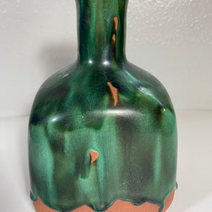 Pode incluir: Um vaso de cerâmica verde com corpo quadrado e pescoço estreito. O vaso tem um efeito de esmalte de gotejamento e uma base de terracota.