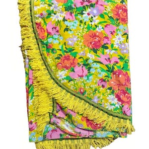 Op de afbeelding: Een ronde deken met bloemenpatroon, met een gele achtergrond en een levendige mix van roze, oranje en witte bloemen. De deken is afgewerkt met een gele franje en een groene rand, wat zorgt voor een vrolijk en kleurrijk ontwerp.