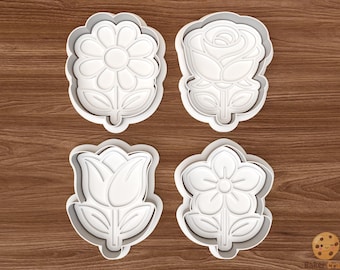 May include: Four white plastic flower-shaped cookie cutters. The cutters include a daisy, a rose, a tulip, and a five-petal flower. The cutters are on a wooden surface.