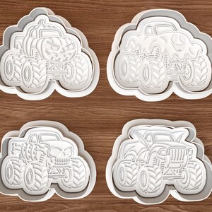 Puede incluir: Un juego de cuatro cortadores de galletas de plástico blanco con forma de camiones monstruo con diseños distintos: uno con calabaza, uno con fantasma, uno con calavera y otro con alas de murciélago. Cada cortador tiene líneas en relieve.