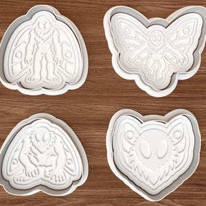 Puede incluir: Un juego de cuatro cortadores de galletas de plástico blanco con diseños en relieve detallados de criaturas similares a polillas en varias poses, incluyendo de pie, volando, agachado y un primer plano de una cara con texturas.