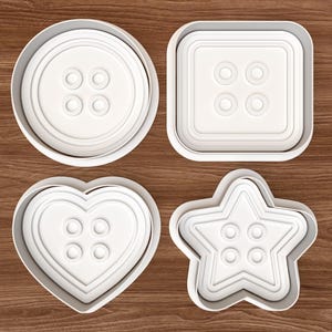 May include: Four white cookie cutters in the shapes of buttons. The shapes include a circle, a square, a heart, and a star. Each cutter has a button design with four holes.