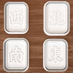 Può includere: Quattro formine per biscotti rettangolari bianche con caratteri cinesi, ciascuna in una cornice rettangolare bianca. I caratteri sono 西, 北, 南 e 東. Le formine sono su una superficie di legno marrone.