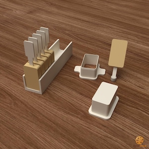 May include: A white rectangular tray holding four tan rectangular blocks with upright white sticks, a white rectangular mold with a hollow center, a solid white rectangular block, and a tan rectangular sign on a white stand.