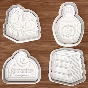 May include: Four white plastic cookie cutters with fantasy themes. Designs include a sleeping dragon on a book, a potion bottle, a sign with the word "Romantasy", and a stack of books with celestial details.